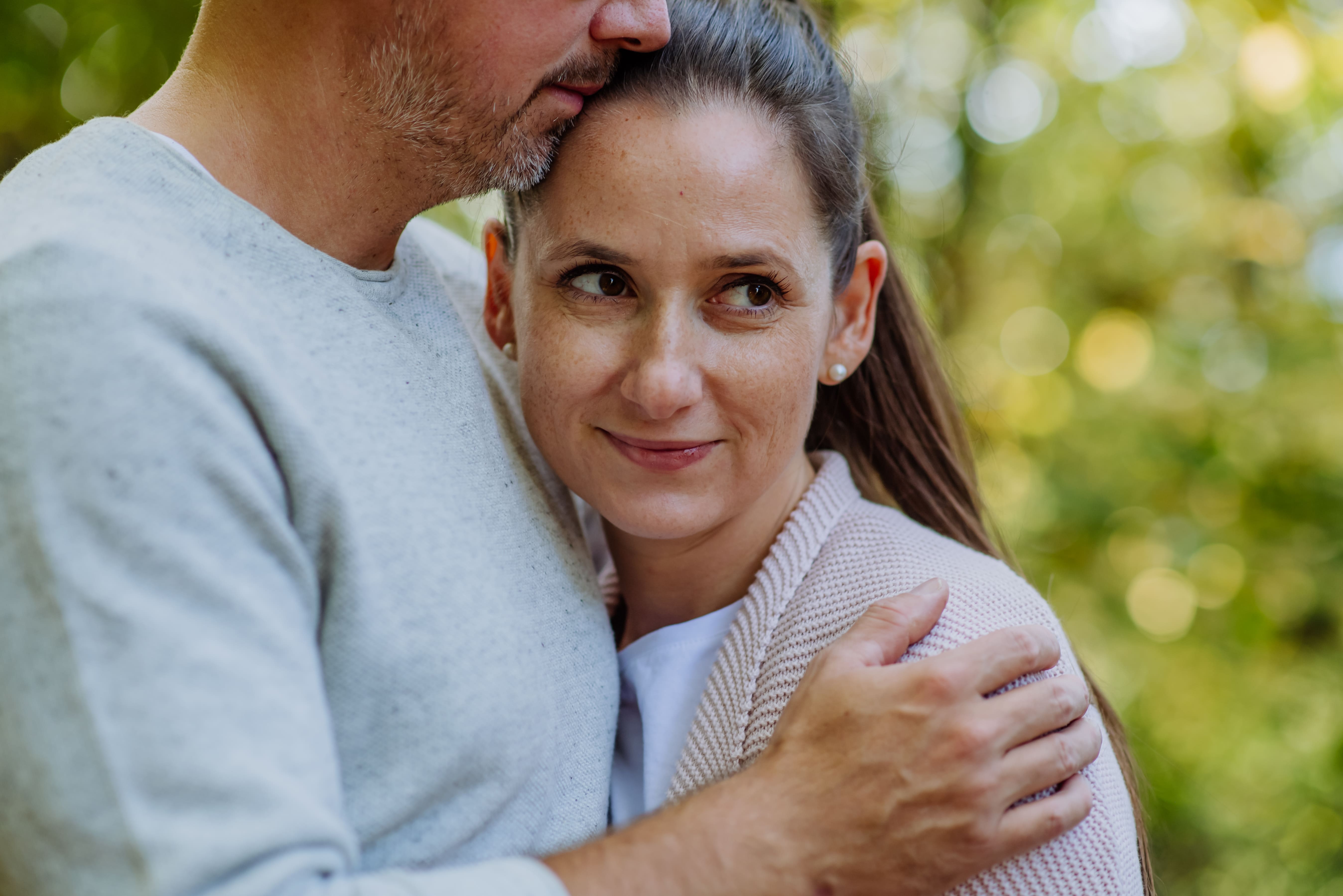 A middle-aged white woman with brown hair looks off to the side and hugs a middle-aged white man.
