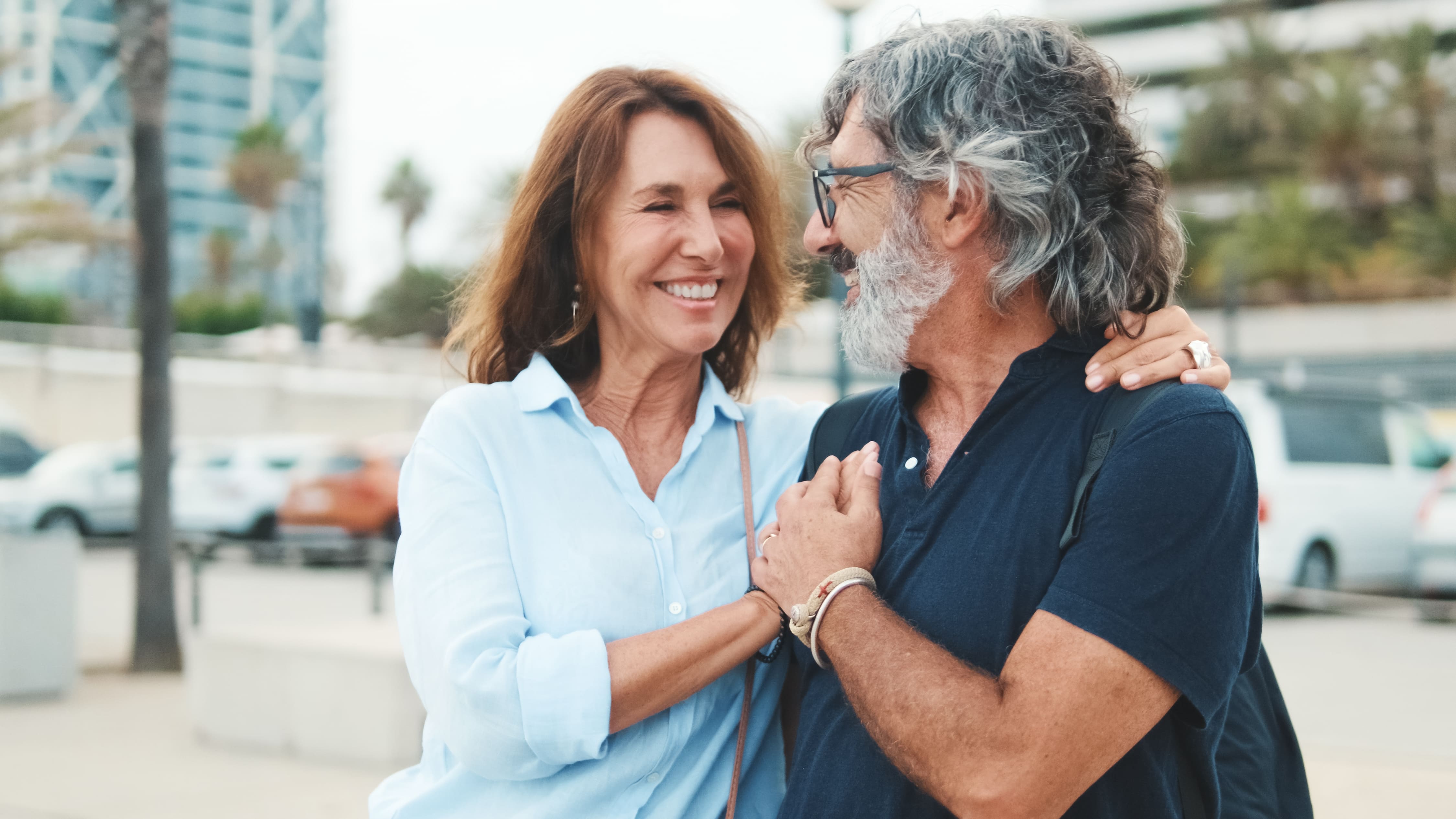 A middle-aged white woman and man clasping hands and smiling at each other.